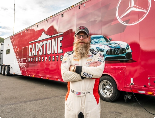 image of John, Owner of Capstone Motorsports in front of his wrapped hauler trailer